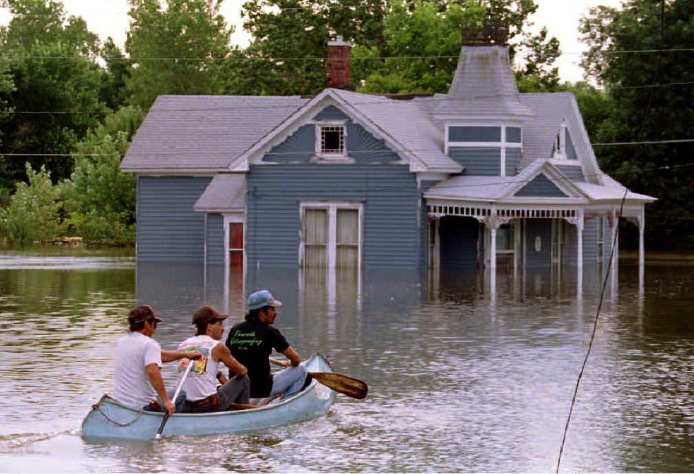 Brothers John (L), Jerry (C) and Ed Tharp canoe through the flooded streets of their town 09 July 1993 after the rising Mississippi River breached the town levee. They row past a historic town home built in the late 19th century.